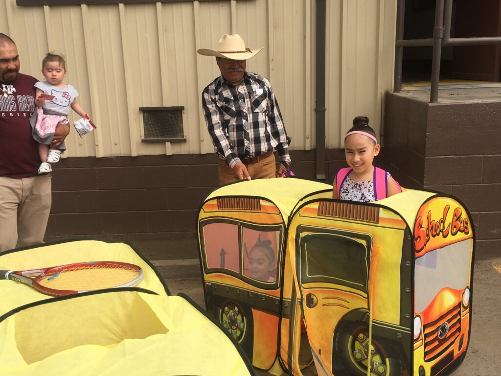 Young girl smiling in toy farm vehicle at agricultural community event promoting farmworker family engagement and workplace opportunities.
